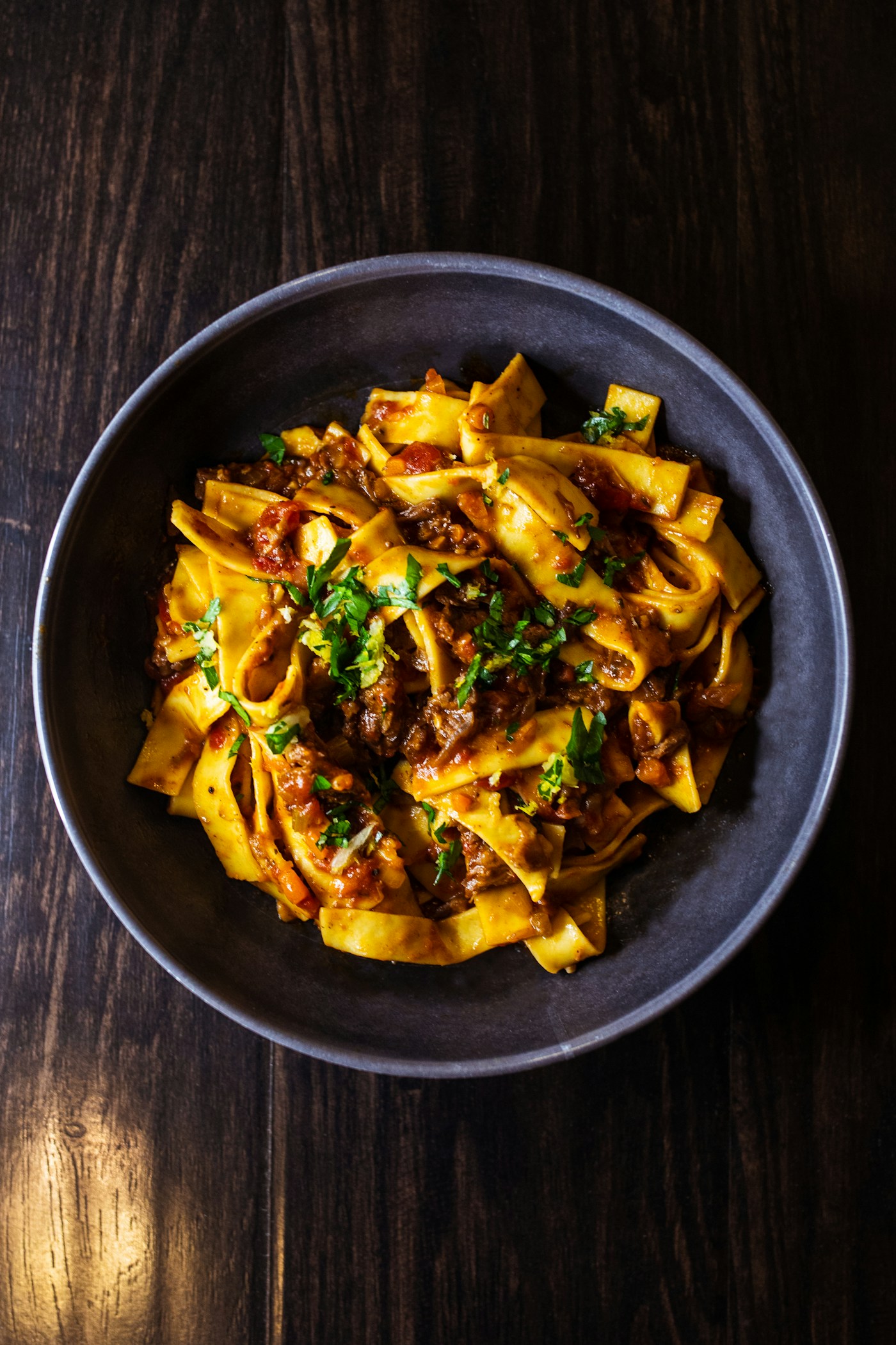 Tagliatelle al ragù dans un bol sombre, persil frais